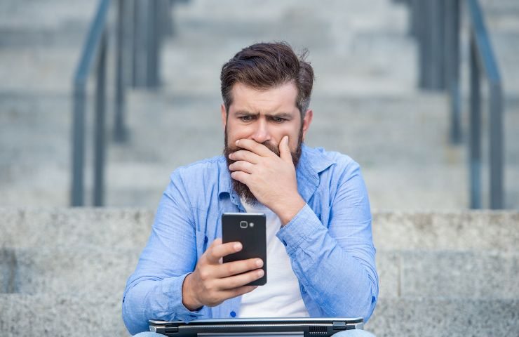 Uomo guarda sorpreso il display del telefono